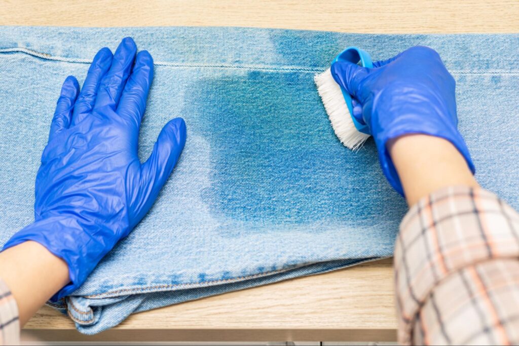 Person using a soft brush to scrub grass stain from jeans