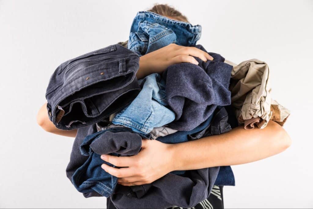 Woman holding pile of dirty work clothes for heavy wash cycle