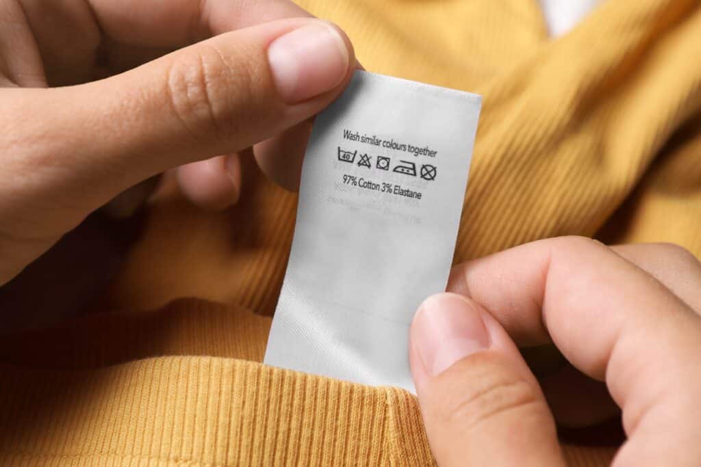 Woman Holding Clothing Label On Yellow Garment Closeup
