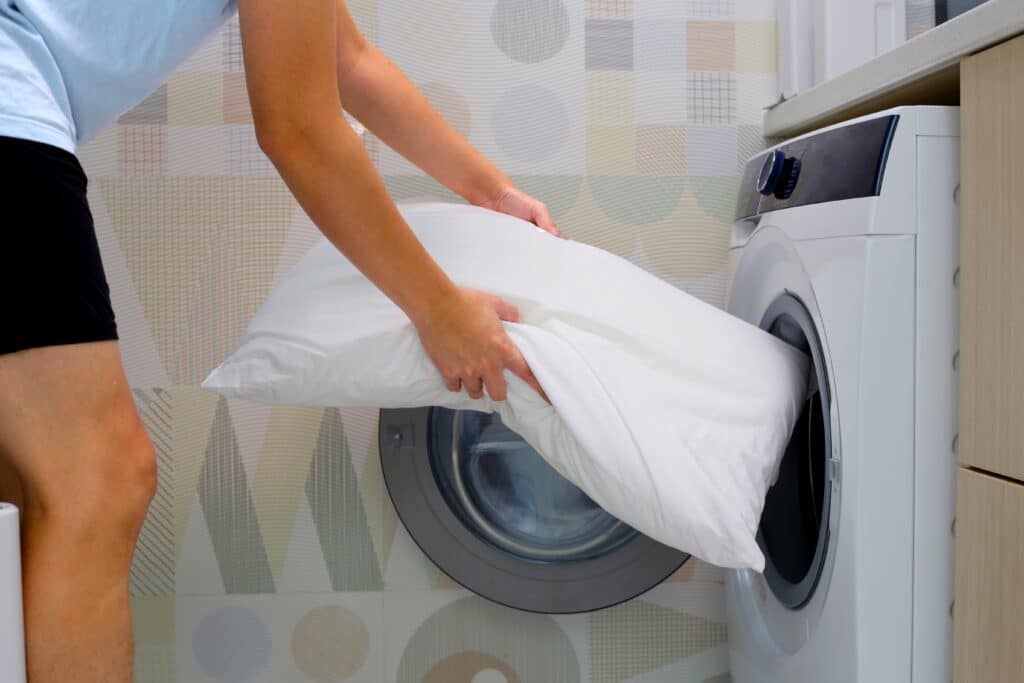 Man putting pillow into washing machine