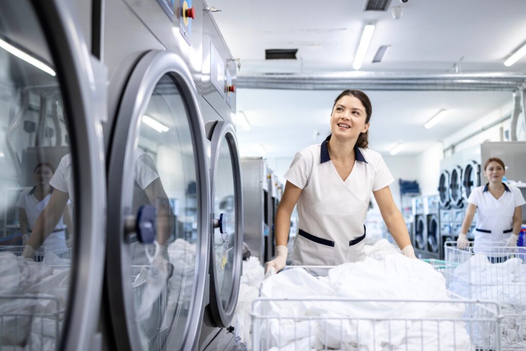 Laundry worker loading white linens into a commercial washer