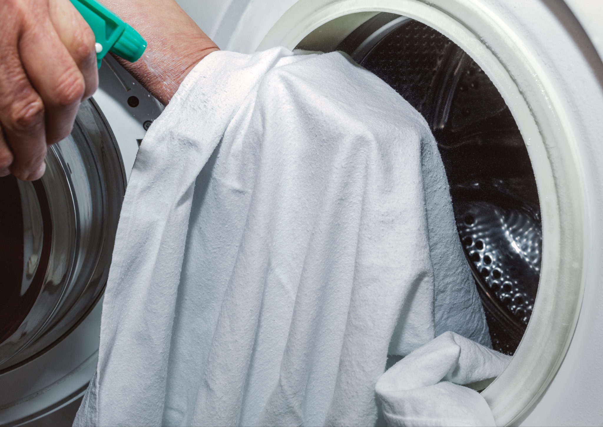 Person placing white sheet in washing machine
