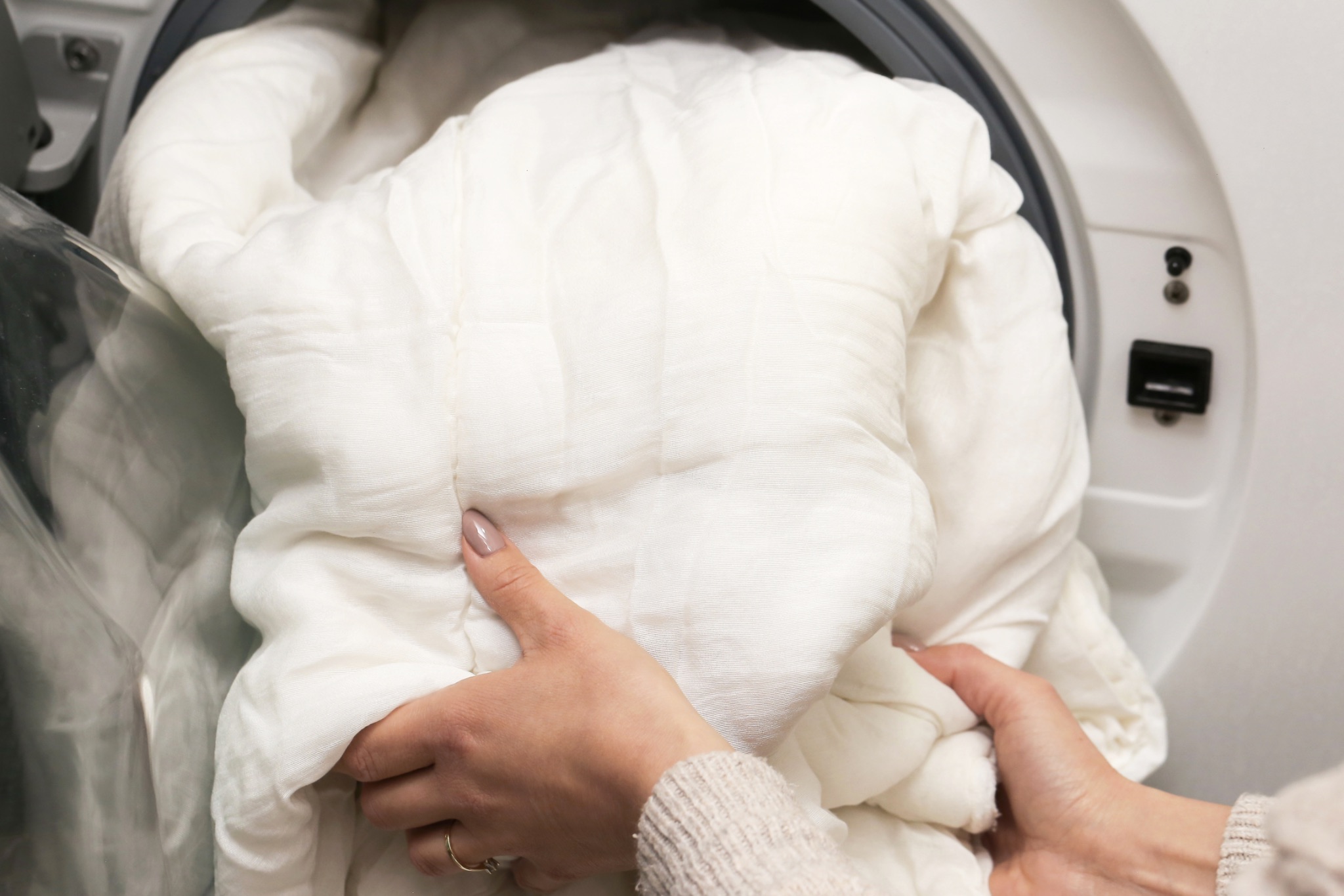 Hands placing white blanket in washing machine